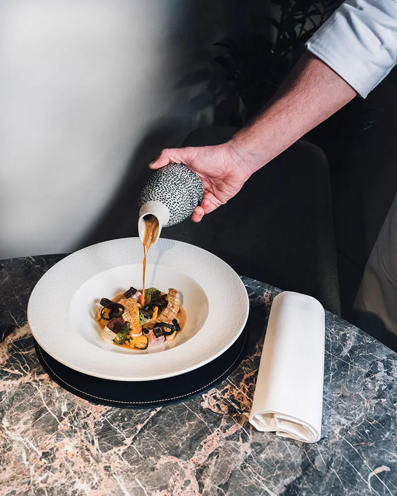 Social media Marketing — Preparazione piatto gourmet guazzetto di pesce su tavolo in marmo nero e grigio al Ristorante Wistèria 1 stella Michelin